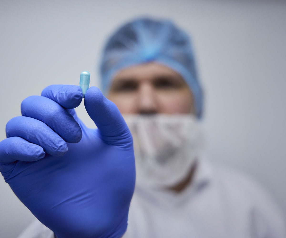 Man wearing lab coat and hair net holding up a capsule